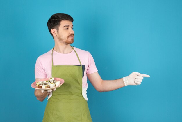 Un joven chef con panecillos recién horneados y apuntando con el dedo.