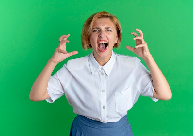 Joven chica rusa rubia molesta le grita a alguien apretando los dedos aislado sobre fondo verde con espacio de copia