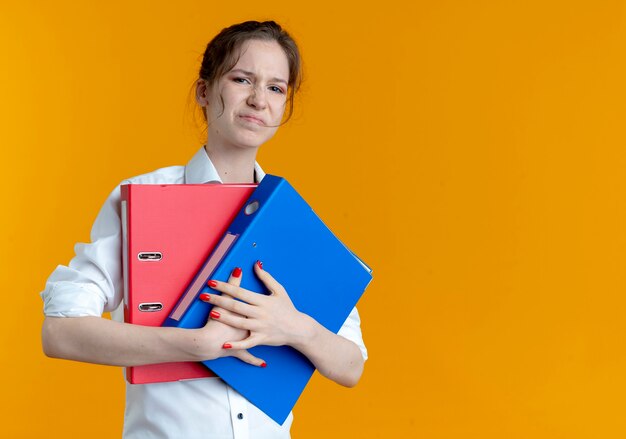 Joven chica rusa rubia molesta tiene carpetas de archivos en naranja con espacio de copia