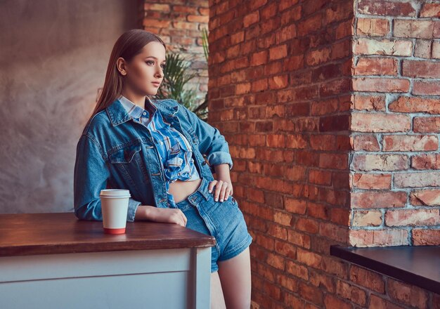 Una joven chica sexy delgada en una chaqueta de jeans y camisa de franela leani