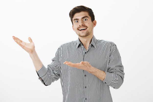 Joven chico europeo feliz con barba y bigote, apuntando hacia la izquierda con las palmas