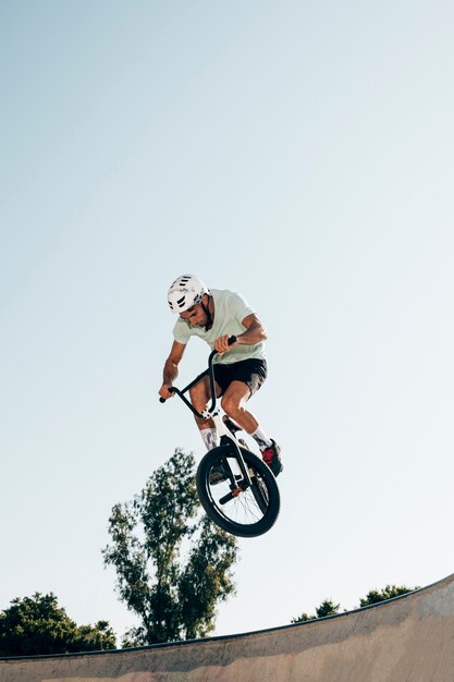 Joven ciclismo en tiro de ángulo bajo skatepark