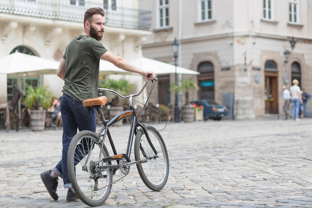 Foto gratuita joven ciclista masculino con su bicicleta en la calle