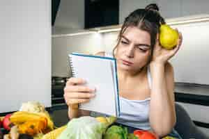 Foto gratuita una joven en la cocina con un cuaderno entre verduras.