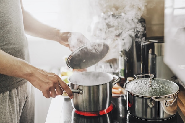 Foto gratuita joven cocinando alimentos frescos en casa y abriendo la tapa de la olla humeante.