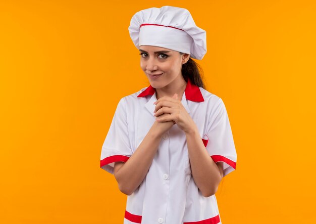 Joven cocinera caucásica alegre en uniforme de chef sostiene su puño aislado en la pared naranja con espacio de copia