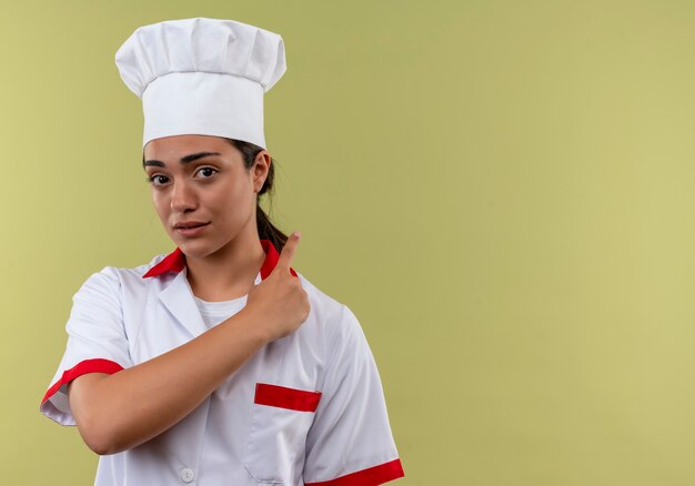 Joven cocinera caucásica confiada en puntos de uniforme de chef aislado en la pared verde con espacio de copia