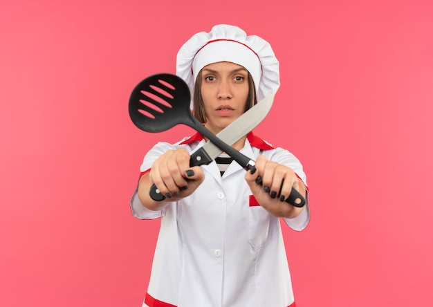 Foto gratuita joven cocinera disgustada en uniforme de chef sosteniendo una espátula y un cuchillo y gesticulando no con ellos a la cámara aislada sobre fondo rosa con espacio de copia