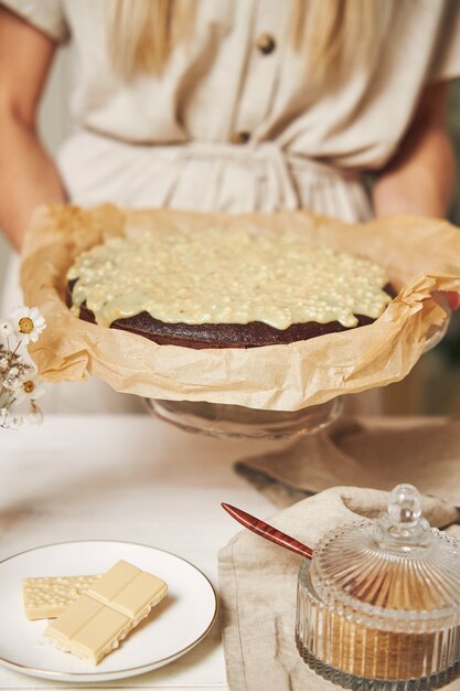 Joven cocinera haciendo un delicioso pastel de chocolate con crema sobre una mesa blanca