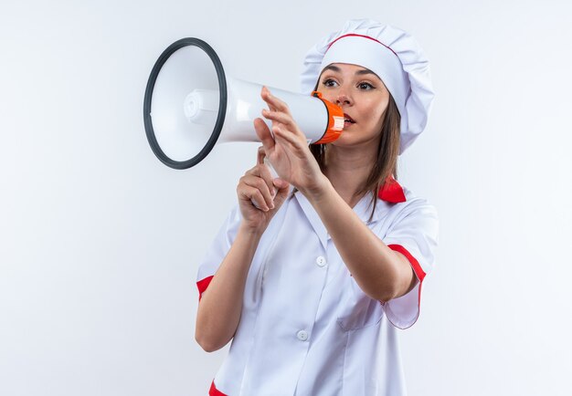 Joven cocinera vistiendo uniforme de chef habla por altavoz aislado sobre fondo blanco.