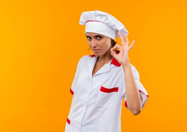 Foto gratuita joven cocinera vistiendo uniforme de chef mostrando gesto okey en pared amarilla aislada con espacio de copia