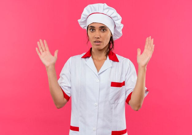 Joven cocinera vistiendo uniforme de chef mostrando el tamaño en la pared rosa aislada con espacio de copia