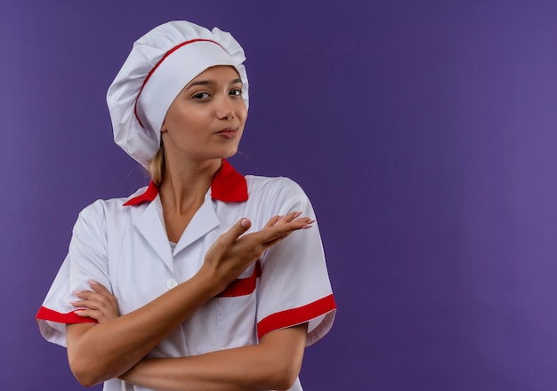 Foto gratuita joven cocinera vistiendo uniforme de chef puntos mano a lado en la pared aislada con espacio de copia