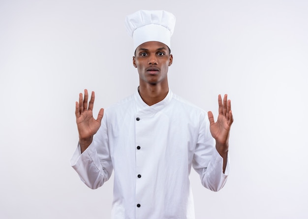 Joven cocinero afroamericano ansioso en uniforme de chef levanta las manos aisladas sobre fondo blanco con espacio de copia