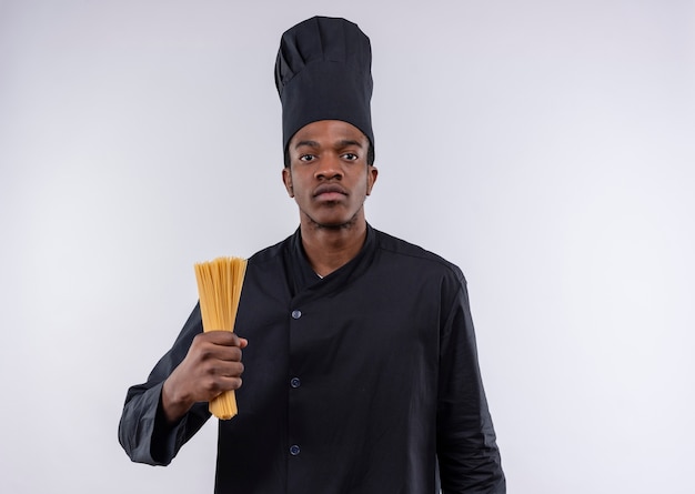Joven cocinero afroamericano confiado en uniforme de chef sostiene un montón de espaguetis aislado sobre fondo blanco con espacio de copia