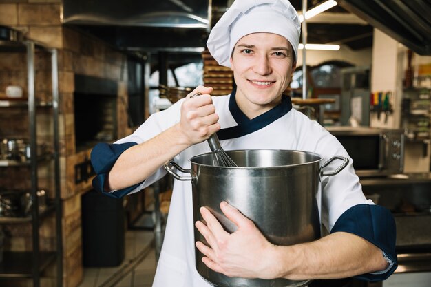 Joven cocinero batiendo algo en una olla con batidor