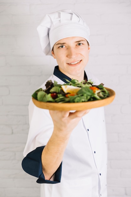 Joven cocinero mostrando placa de madera con ensalada