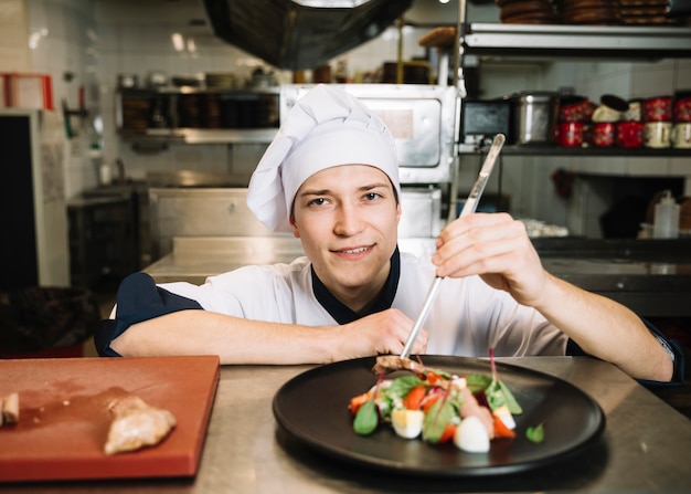 Joven cocinero preparando ensalada con carne en la mesa