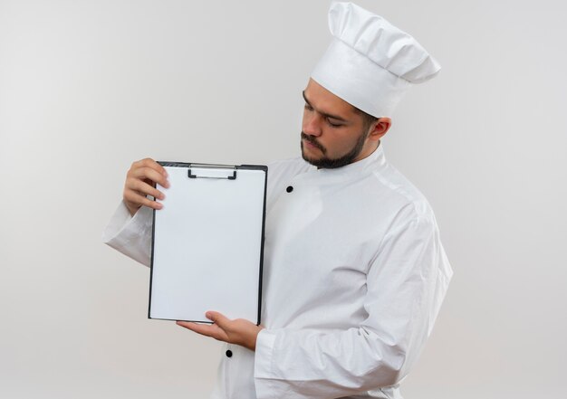 Joven cocinero en uniforme de chef mostrando y mirando el portapapeles