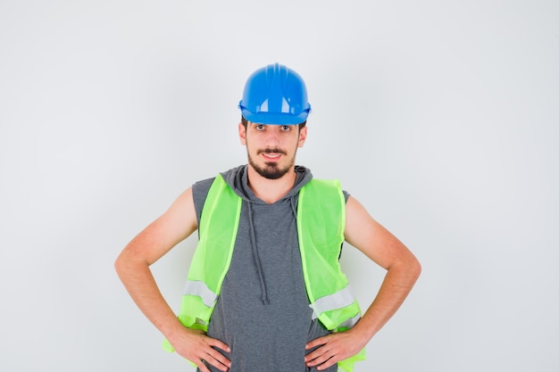 Foto gratuita joven cogidos de la mano en la cintura en uniforme de construcción y mirando feliz