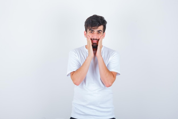 Joven cogidos de la mano en las mejillas en camiseta y luciendo lindo