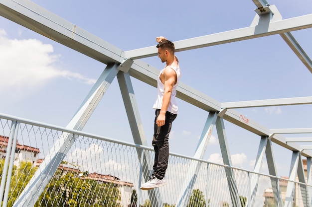 Joven colgando con su mano en el puente