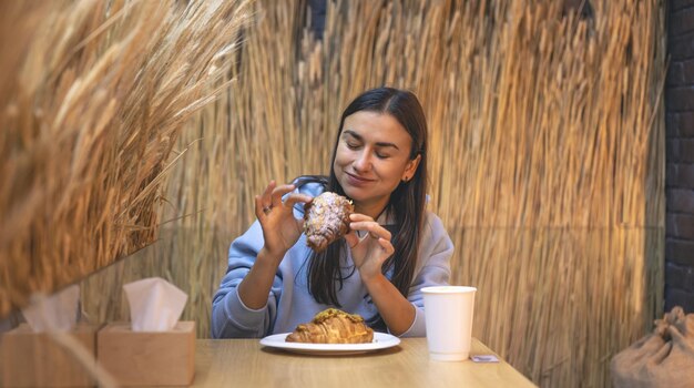 Una joven come croissants con café en una cafetería.