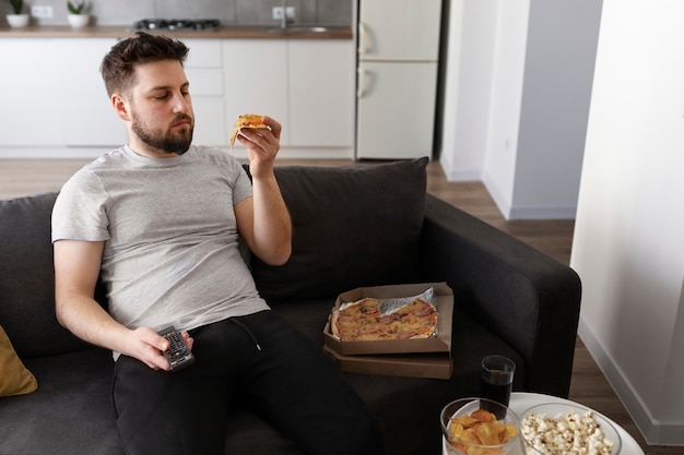 Joven comiendo comida chatarra en casa en el sofá