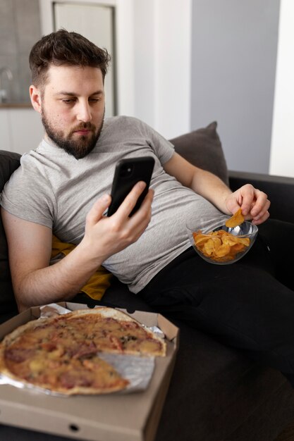 Joven comiendo comida chatarra en casa en el sofá