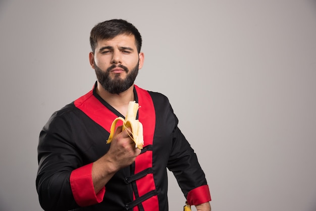 Foto gratuita joven comiendo un plátano en la pared gris.