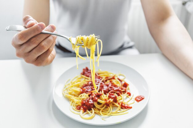 Joven comiendo sabroso espagueti con salsa de tomate. De cerca.