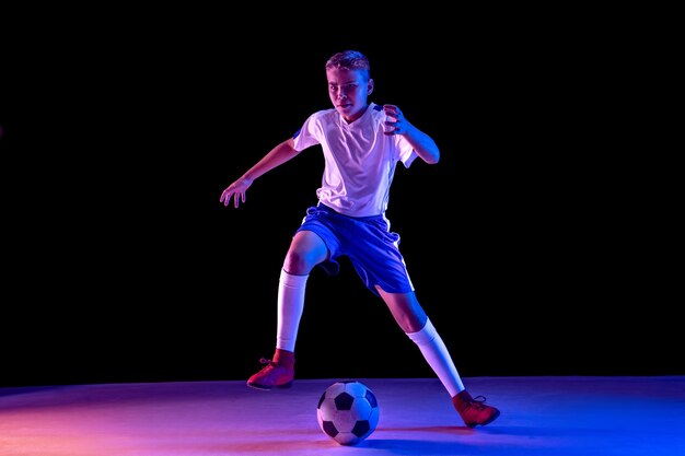 Joven como jugador de fútbol o fútbol en la pared oscura del estudio