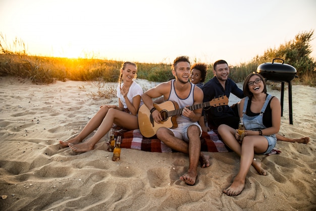 Joven compañía de amigos regocijándose, descansando en la playa durante el amanecer