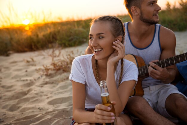 Joven compañía de amigos regocijándose, descansando en la playa durante el amanecer