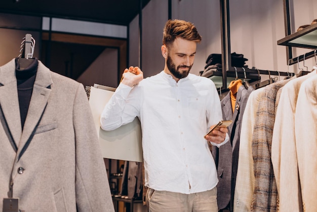 Joven comprando en la tienda de ropa masculina y hablando por teléfono