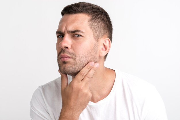 Joven comprobando su rostro de pie contra la pared blanca