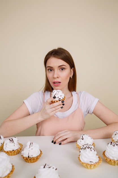 Foto gratuita joven concentrada posando mientras está sentado cerca de cupcakes