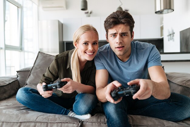 Joven concentrado hombre y mujer jugando videojuegos en la sala de estar