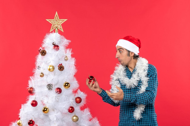 Joven concentrado con sombrero de santa claus en una camisa azul a rayas y sosteniendo accesorio decotaion permanente