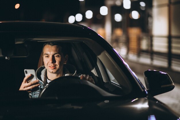 Joven conduciendo su automóvil por la noche y hablando por teléfono