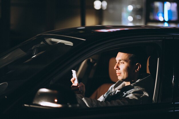 Joven conduciendo su automóvil por la noche y hablando por teléfono