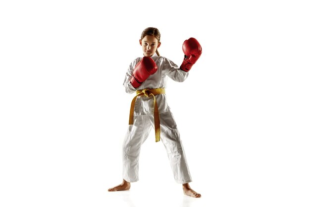 Joven confiado en kimono practicando combate cuerpo a cuerpo, artes marciales. Joven luchadora con entrenamiento de cinturón amarillo en la pared blanca. Concepto de estilo de vida saludable, deporte, acción.