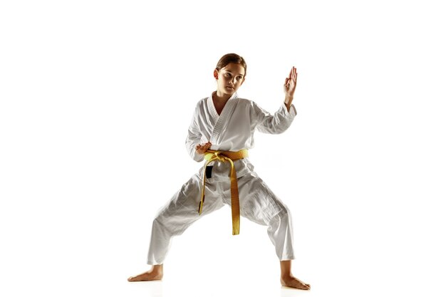 Joven confiado en kimono practicando combate cuerpo a cuerpo, artes marciales. Joven luchadora con entrenamiento de cinturón amarillo en la pared blanca. Concepto de estilo de vida saludable, deporte, acción.