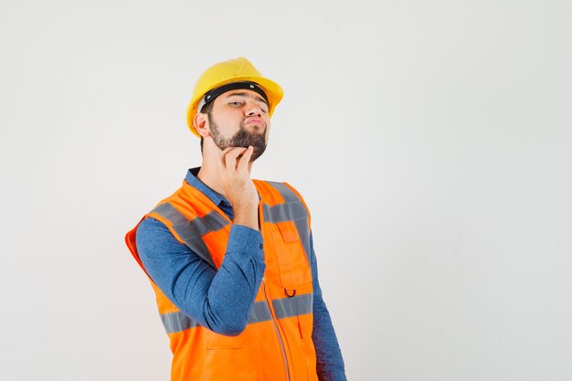 Joven constructor en camisa, chaleco, casco rascándose la barba y luciendo elegante, vista frontal.