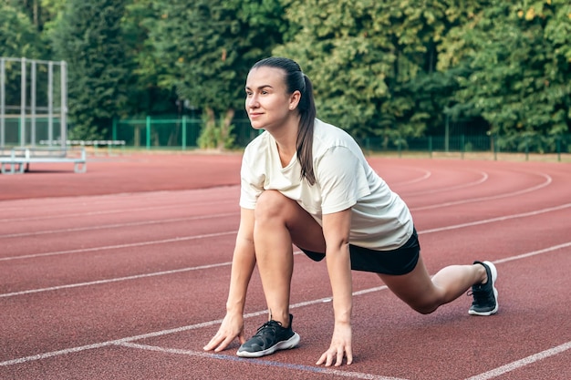 Foto gratuita una joven corredora en posición inicial en la pista de atletismo mientras hace ejercicio