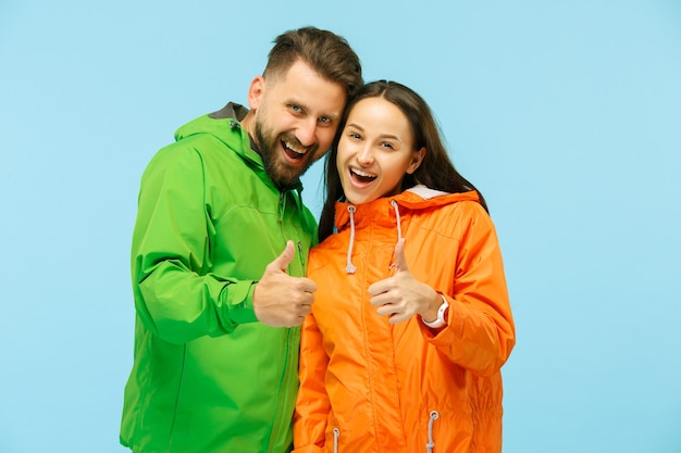 El joven couplel sorprendido posando en el estudio en chaquetas de otoño aislado en azul