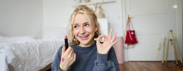 Joven creadora de contenido de blogger que muestra lápiz labial y un signo de mano de "okay" recomendando productos de belleza