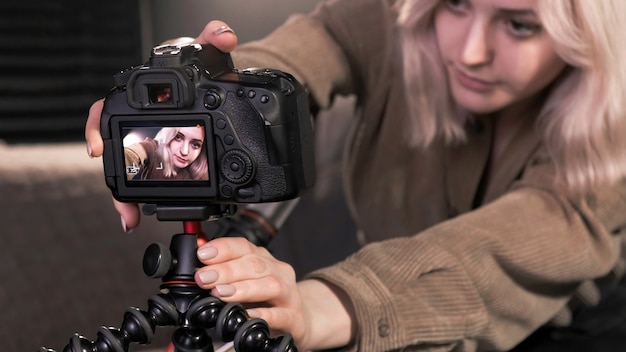 Joven creadora de contenido chica rubia poniendo una cámara en un trípode y filmándose a sí misma hablando para vlog
