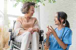 Foto gratuita joven cuidadora asiática cuidando a su paciente anciano en la guardería para personas mayores paciente discapacitado en silla de ruedas en el hospital hablando con una enfermera amigable y luciendo alegre enfermera dando vueltas paciente mayor