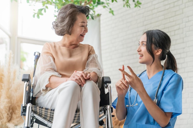 Joven cuidadora asiática cuidando a su paciente anciano en la guardería para personas mayores Paciente discapacitado en silla de ruedas en el hospital hablando con una enfermera amigable y luciendo alegre Enfermera dando vueltas Paciente mayor